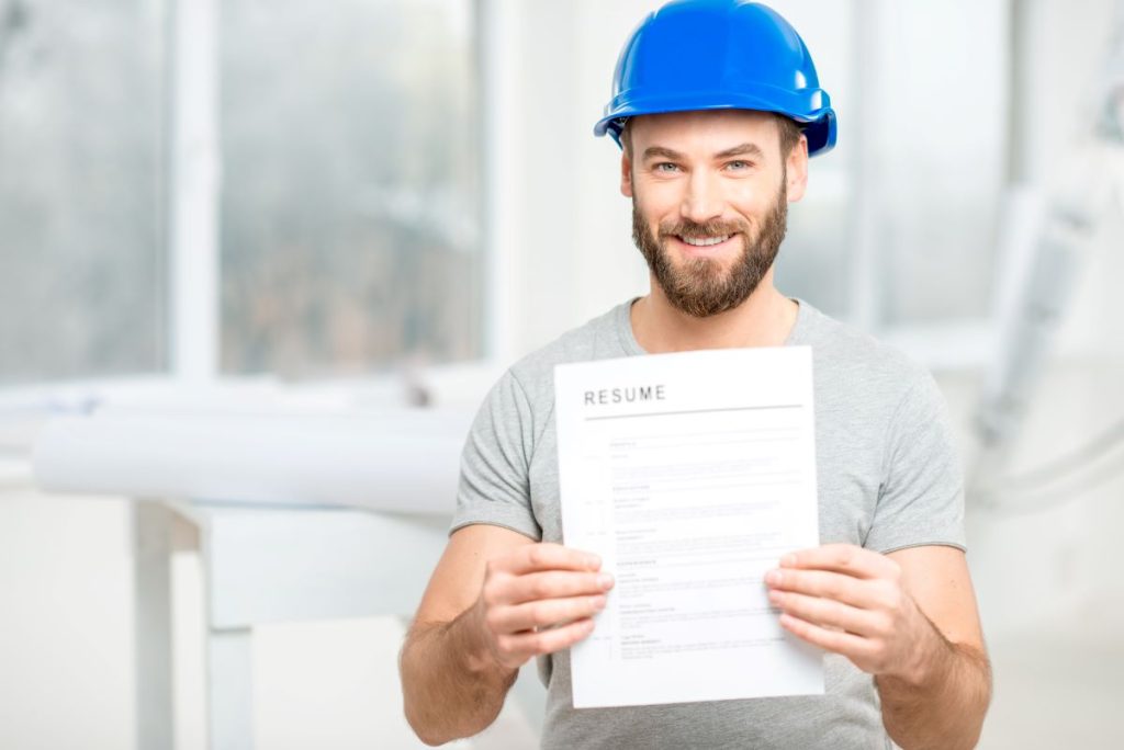 Un travailleur de la construction tient un exemple de CV dans ses mains.